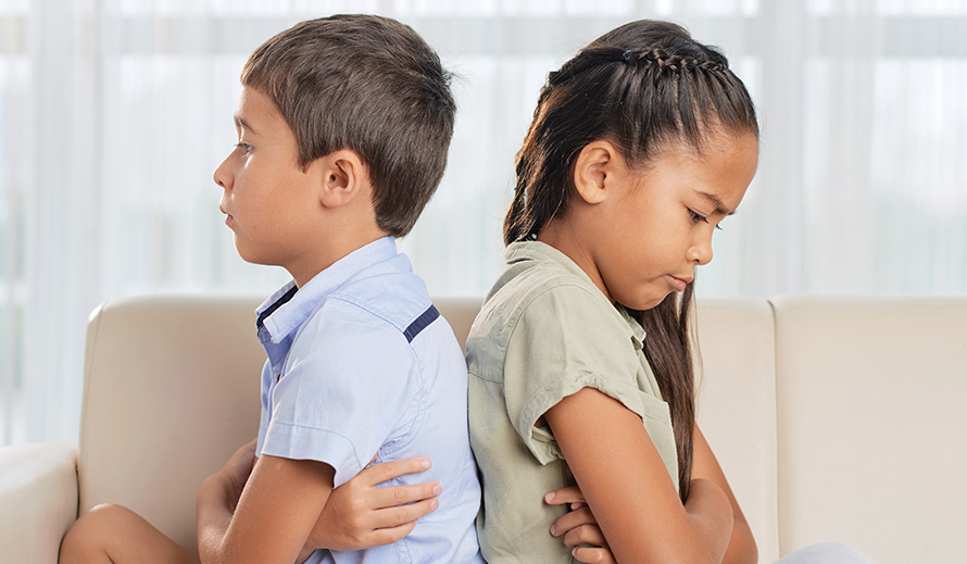 Upset brother and sister sit back-to-back with arms crossed. 