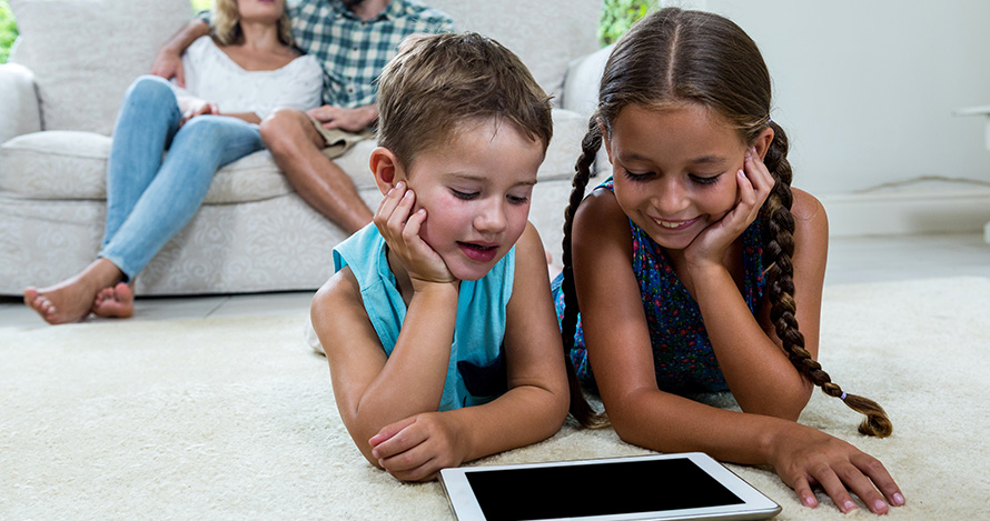 Two young girls spend some screen time at home while parents look on. 