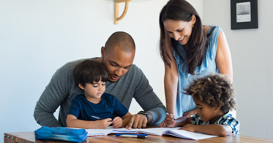 A diverse family sits around a table reading. 